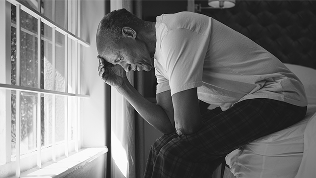 man sitting on edge of bed with head in hand