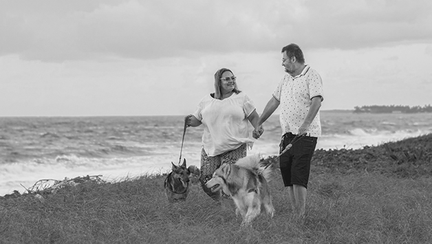 man and woman walking dog by ocean