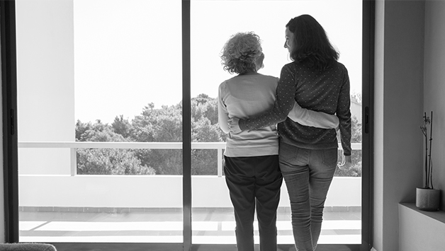 senior mother and adult daughter hugging in front of window