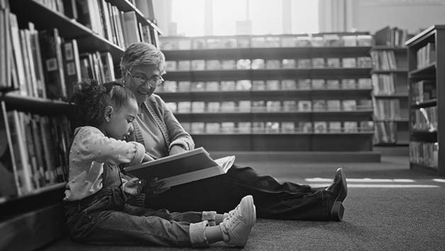 senior woman sitting and reading with child in library