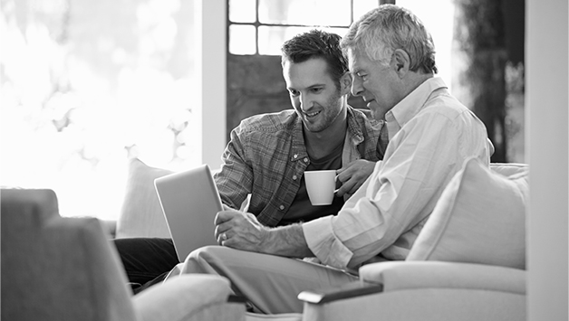 father and adult son sitting on sofa planning senior care